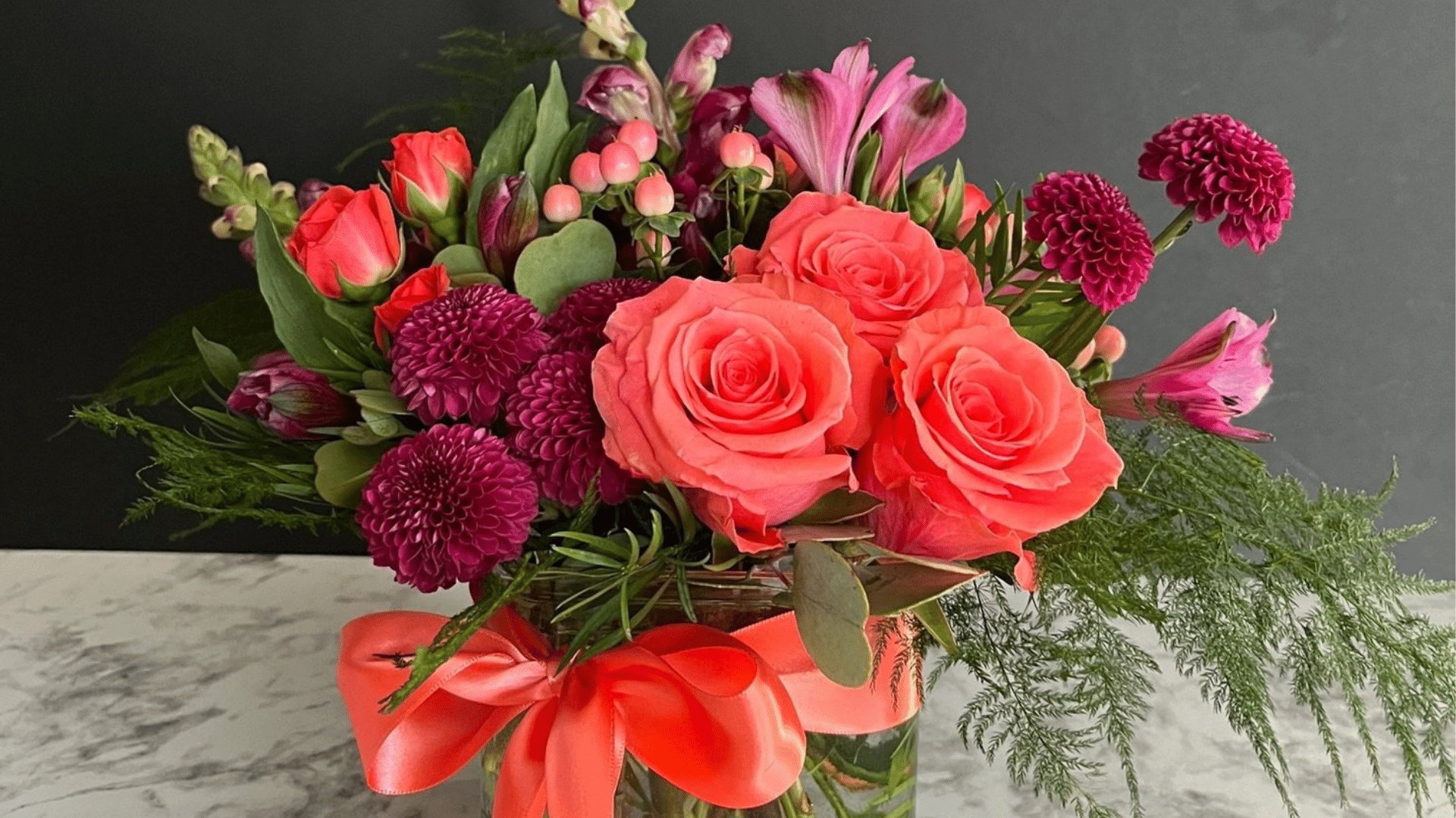 bouquet of flowers made up of coral colored roses, burgundy dahlias, and greenery